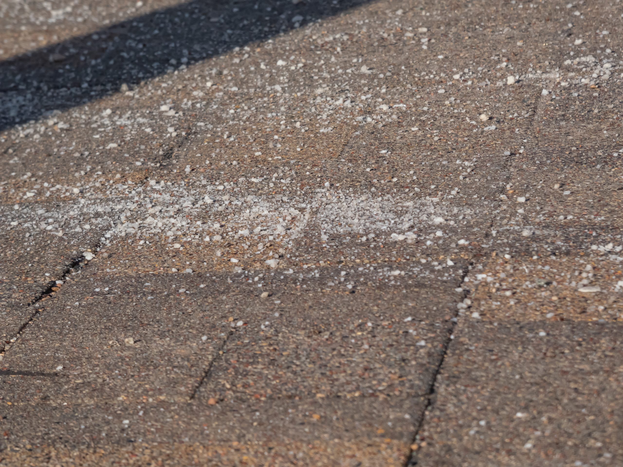 Salt grains on icy sidewalk surface in the winter. Applying salt to keep roads clear and people safe in winter weather from ice or snow